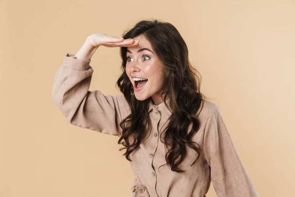 Image of excited brunette woman smiling and looking aside isolated over beige background - Zdjęcie, obraz