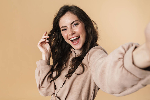 Εικόνα του χαρούμενα χαριτωμένο γυναίκα γέλιο και λήψη selfie φωτογραφία απομονώνονται σε μπεζ φόντο - Φωτογραφία, εικόνα