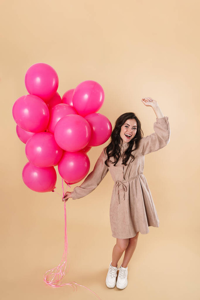 Image of excited cute woman laughing and dancing with pink balloons isolated over beige background - Foto, immagini