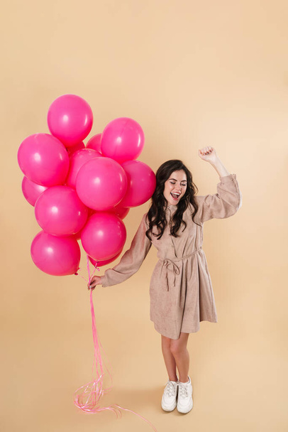 Image of excited cute woman laughing and dancing with pink balloons isolated over beige background - Foto, Imagem