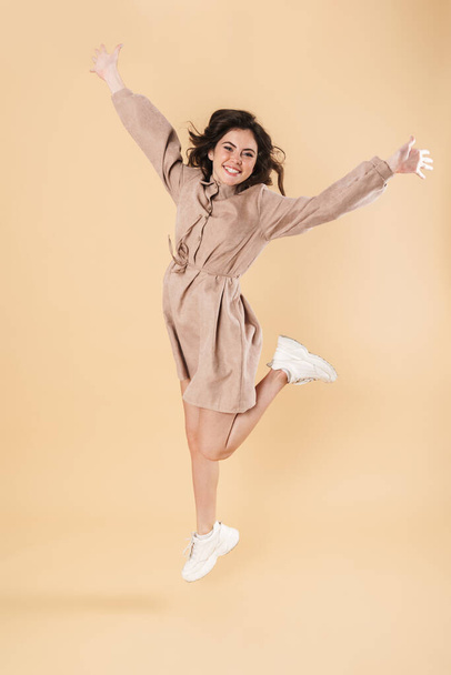 Image of excited caucasian woman smiling and jumping on camera isolated over beige background - Φωτογραφία, εικόνα