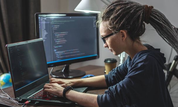 現代の若い女性プログラマーは自宅でラップトップ上でプログラムコードを書いています。ITプロフェッショナルとしてのリモートワーク。ソフトウェア開発の概念. - 写真・画像
