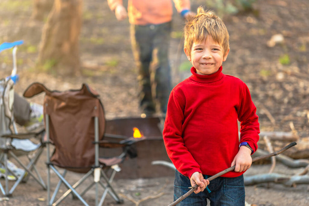 Gelukkig kind met een stok terwijl het vuur brandt op Kuitpo bos camping tijdens de winter schoolvakanties in Zuid-Australië - Foto, afbeelding
