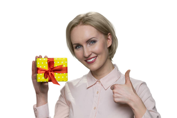 Feliz sorrindo mulher loira segurando caixa de presente e fazendo gesto ok
. - Foto, Imagem