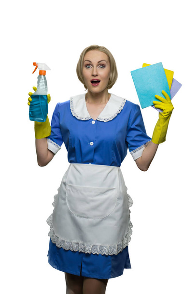 Surprised maid with open mouth holding cleaner spray and sponge cloths on white background. - Photo, Image