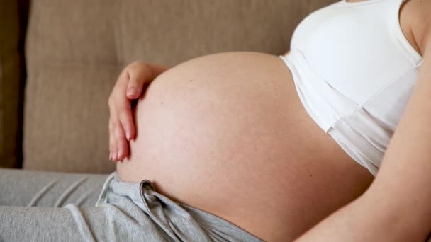 Een zorgzame moeder streelt een naakte zwangere buik met twee handen, op lichte kamer. Een zwangere vrouw streelt een grote buik in de zonnige zomerdag. - Video