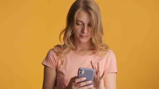 Attractive blond girl happily using smartphone on camera over colorful background - Filmati, video