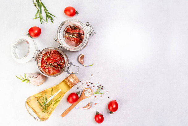 Zongedroogde tomaten met knoflook, oregano, olijfolie in een pot op een lichte tafel, banner, menukaart plaats voor tekst, bovenaanzicht. - Foto, afbeelding