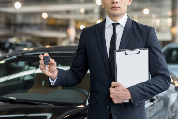 Young car salesman standing at the dealership and holding a key - Foto, Imagem