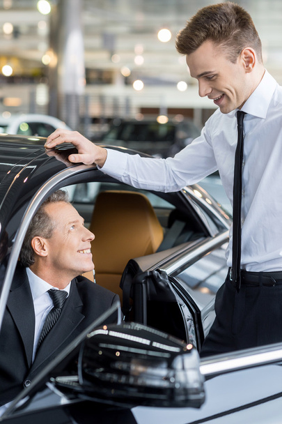 Man sitting at the front seat of the car and talking to the car salesman - Foto, Imagen