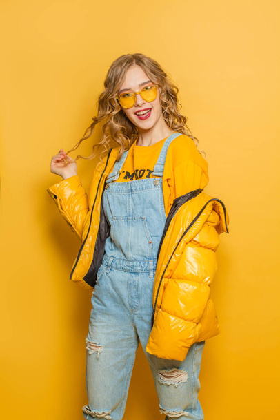 Cute woman in winter jacket on bright yellow background - Фото, изображение