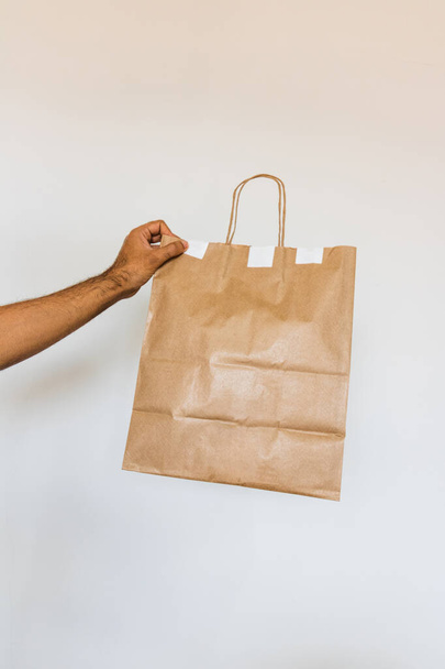 Sostiene una bolsa de papel aislada. Entrega a casa comida aplicación concepto imagen
. - Foto, Imagen