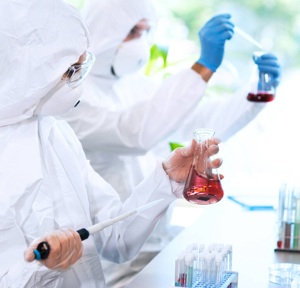 Scientists in protection suits and masks working in research lab using laboratory equipment: microscopes, test tubes. Biological hazard, pharmaceutical discovery, bacteriology and virology concept. - Foto, afbeelding
