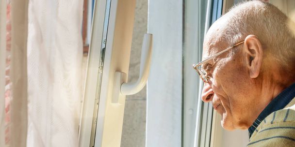 bald old man stands at window looking outside closeup - Fotó, kép