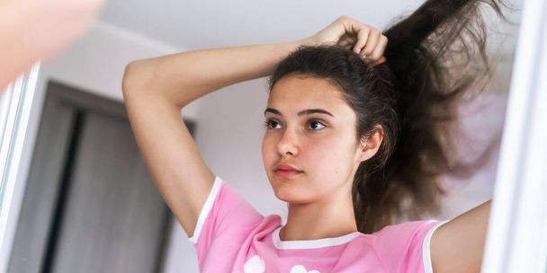 brunette schoolgirl in pink makes ponytail hairstyle closeup - Foto, afbeelding