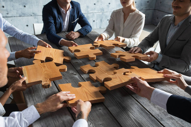 Business people team sitting around meeting table and assembling wooden jigsaw puzzle pieces unity cooperation ideas concept - Foto, afbeelding