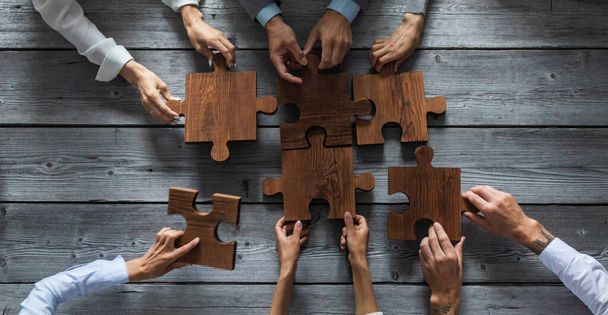 Business people team sitting around meeting table and assembling wooden jigsaw puzzle pieces unity cooperation ideas concept - Photo, image