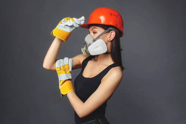 Construction girl in an orange hard hat and protective construction mask, for heavy work where you need protection from inhaling harmful gases and sprayed particles in the air. the concept of advertising - Zdjęcie, obraz