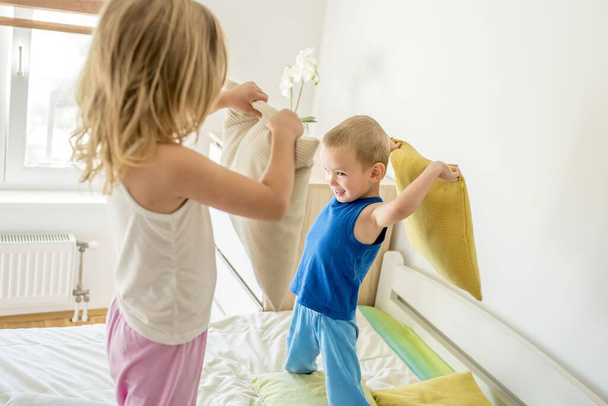 A girl and a boy smiling and having a pillow fight on a bed - Foto, Imagen