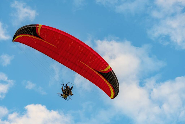 Red dome of a motor paraglider flying on a background of blue cloudy summer sky. Tandem on a paraglider high in the sky. - Fotó, kép