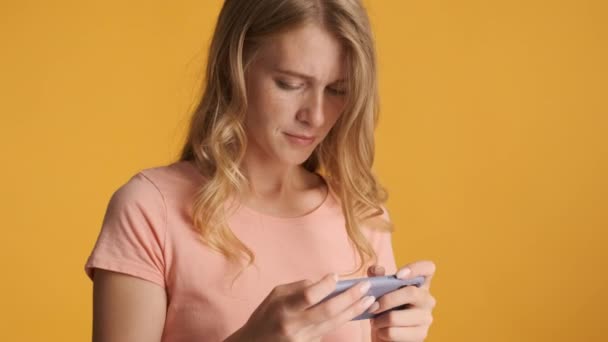 Young concentrated blond woman playing in game on smartphone and happily smiling over colorful background - Video