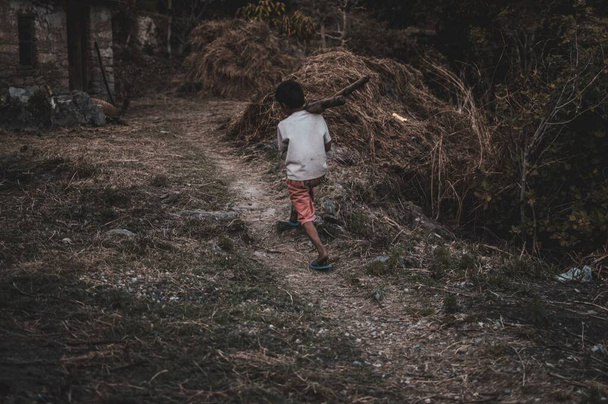 A selective focus shot of a young boy carrying heavy tree logs in a rural area - Φωτογραφία, εικόνα