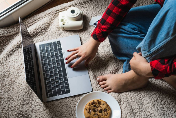 A horizontal shot of a female sitting on a blanket with her laptop and a cookie - Foto, afbeelding
