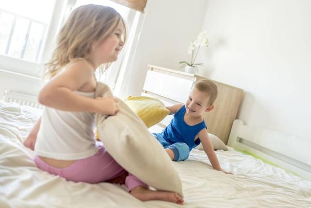 Two Caucasian children playing together with pillows on the bed - Fotó, kép