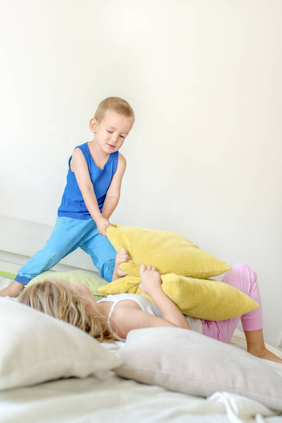 Μια κάθετη λήψη με ξανθά παιδιά να παίζουν με μαξιλάρια στο κρεβάτι στο δωμάτιο - Φωτογραφία, εικόνα