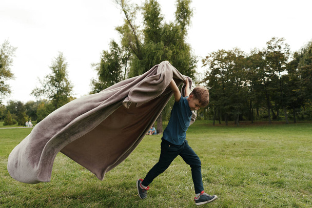 Wesoły chłopak biegający z latającym kocem w parku - Zdjęcie, obraz