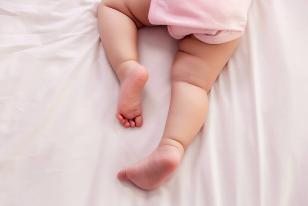 Adorable innocent baby try to crawling on bed that the first time infant baby crawl. Lovely toddler girl wear pink baby dress. Toddler child trying to use leg for lifting legs and body. Close up legs - Foto, Imagen