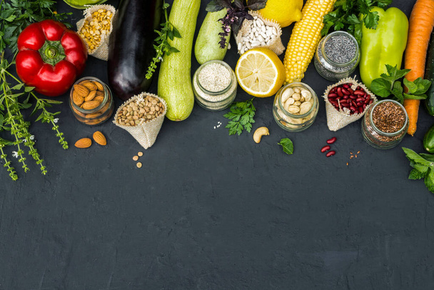 Vegetarisch concept groenten noten en granen op een zwarte achtergrond. Wortel, peper, aubergine, peterselie, pompoen, komkommer, merg, citroen, - Foto, afbeelding