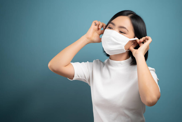 青い背景に隔離されたウイルスや病気から保護するための保護マスクを身に着けているアジアの女性。COVID-19,コロナウイルスの概念. - 写真・画像