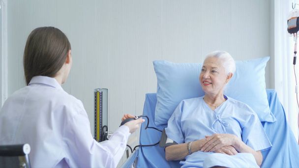 Happy woman doctor checking blood pressure test of sick old female senior elderly patient lying in bed in hospital ward room in medical, and healthcare treatment concept. Caucasian white people. - Foto, Bild