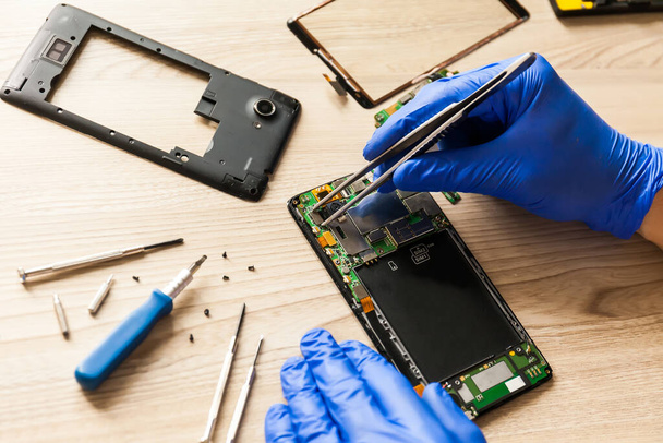 The technician repairing the smartphone's motherboard in the workshop on the table. Concept of computer hardware, mobile phone, electronic, repairing, upgrade and technology. - Photo, image