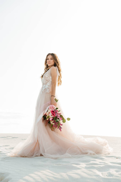 История любви красивой пары в розовом свадебном роскошном платье с букетом в пустыне Фара, песке, дюнах - Фото, изображение