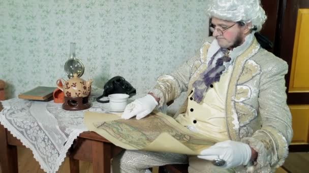 Mies keskiaikaisissa vaatteissa katsoo vanhaa karttaa ja nyökkää
 - Materiaali, video