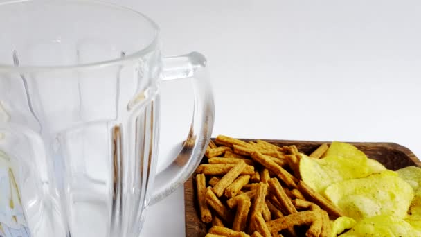 Pouring beer into a glass mug on the background of a plate with chips and crackers - Video, Çekim