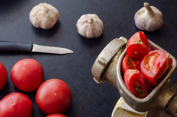Handmatige vintage vleesmolen en rijpe groenten op tafel. Rode tomaten en een knoflookkop. Zelfgemaakte tomatensaus maken. Gebruik van verouderd keukengerei. - Foto, afbeelding
