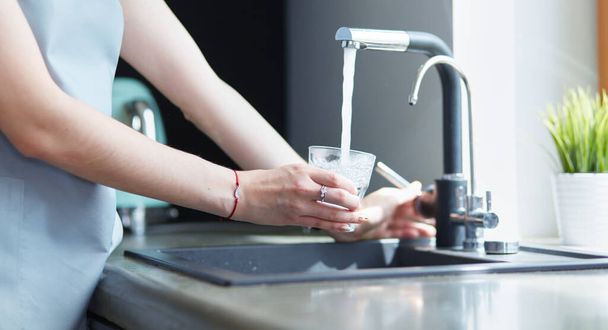 Human hand holding glass pouring fresh drink water at kitchen faucet - Фото, зображення