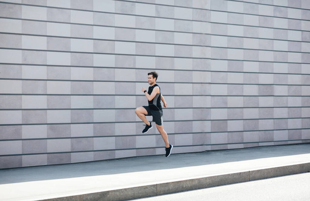 Jogging with jumping. Guy runs at path near gray brick wall in city - 写真・画像