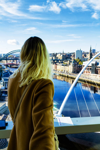 Blondynka stojąca i patrząca na Tyne River z mostami w Newcastle upon Tyne, Anglia, Wielka Brytania - Zdjęcie, obraz