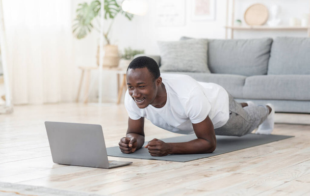 家でノートパソコンを使って運動してる若い黒人が - 写真・画像
