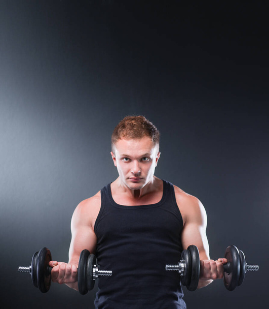 Closeup of a muscular young man lifting weights on dark background - 写真・画像