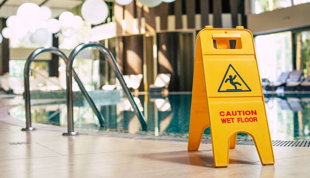 Yellow sign of wet floor plate is near the swimming pool. - Photo, image
