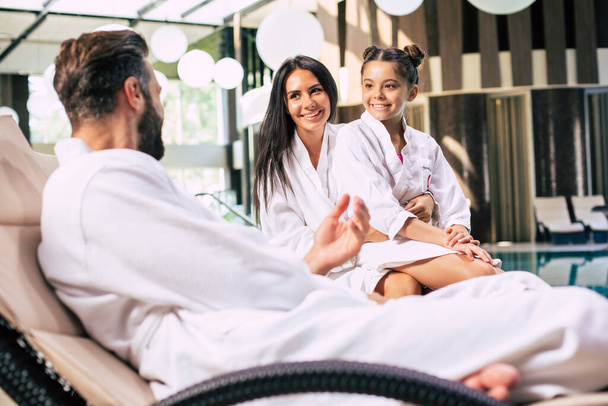 Happy beautiful family in bathrobes are joyful together while sitting in the spa salon - Фото, изображение