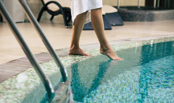 Photo of female legs while she trying the water in hotel pool. Vacation and recreation in the spa - Fotoğraf, Görsel
