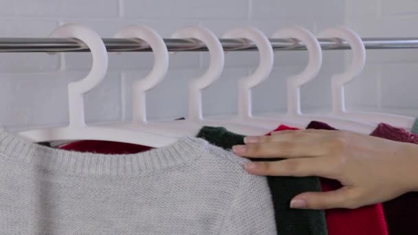 Knitted sweaters on hangers. Close-up of female hands plucked a hanger with clothes. Woman's hands run across a rack of clothes. Woman's hand smoothing a colorful clothes. Shopping in a Store. - Footage, Video