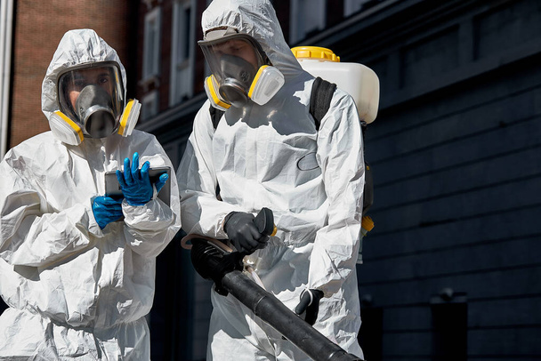 Храбрые уборщики в костюме, маске и перчатках, проводят дезинфекцию от коронавируса - Фото, изображение