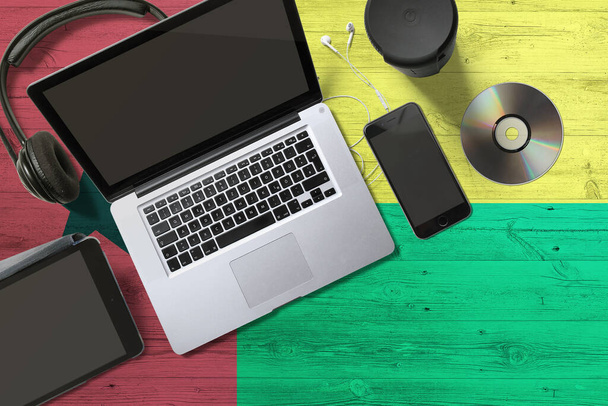 Guinea flag on national background wooden table. Portable devices concept. Cd, headphones, tablet, notebook. Digital media theme. - Fotografie, Obrázek